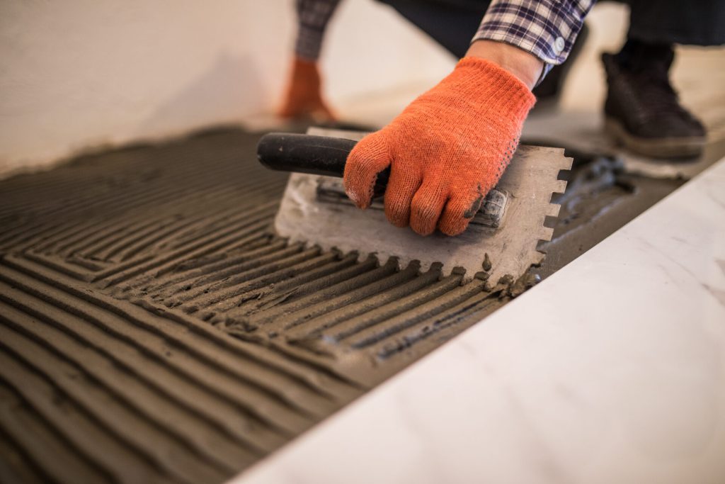 Tile adhesive being applied with a notched trowel during tile installation.
